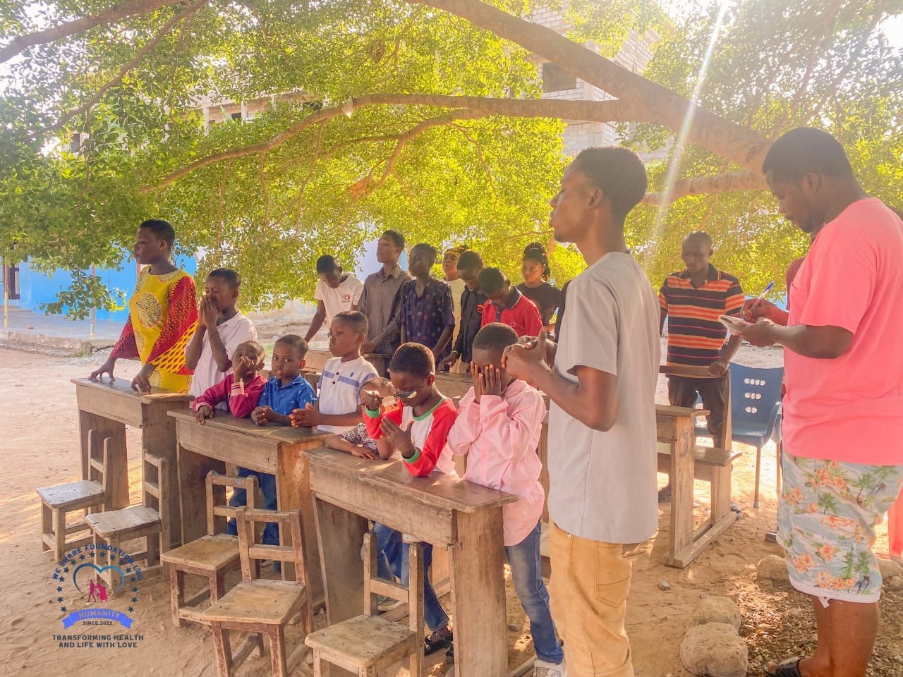 Children gathered under a tree during a We Share Foundation outreach